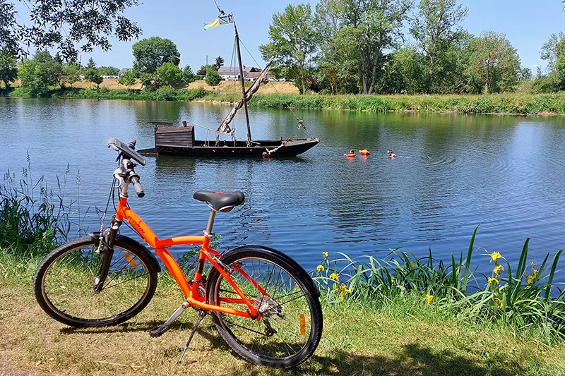 vélo orange devant une rivière avec un petit bateau en bois